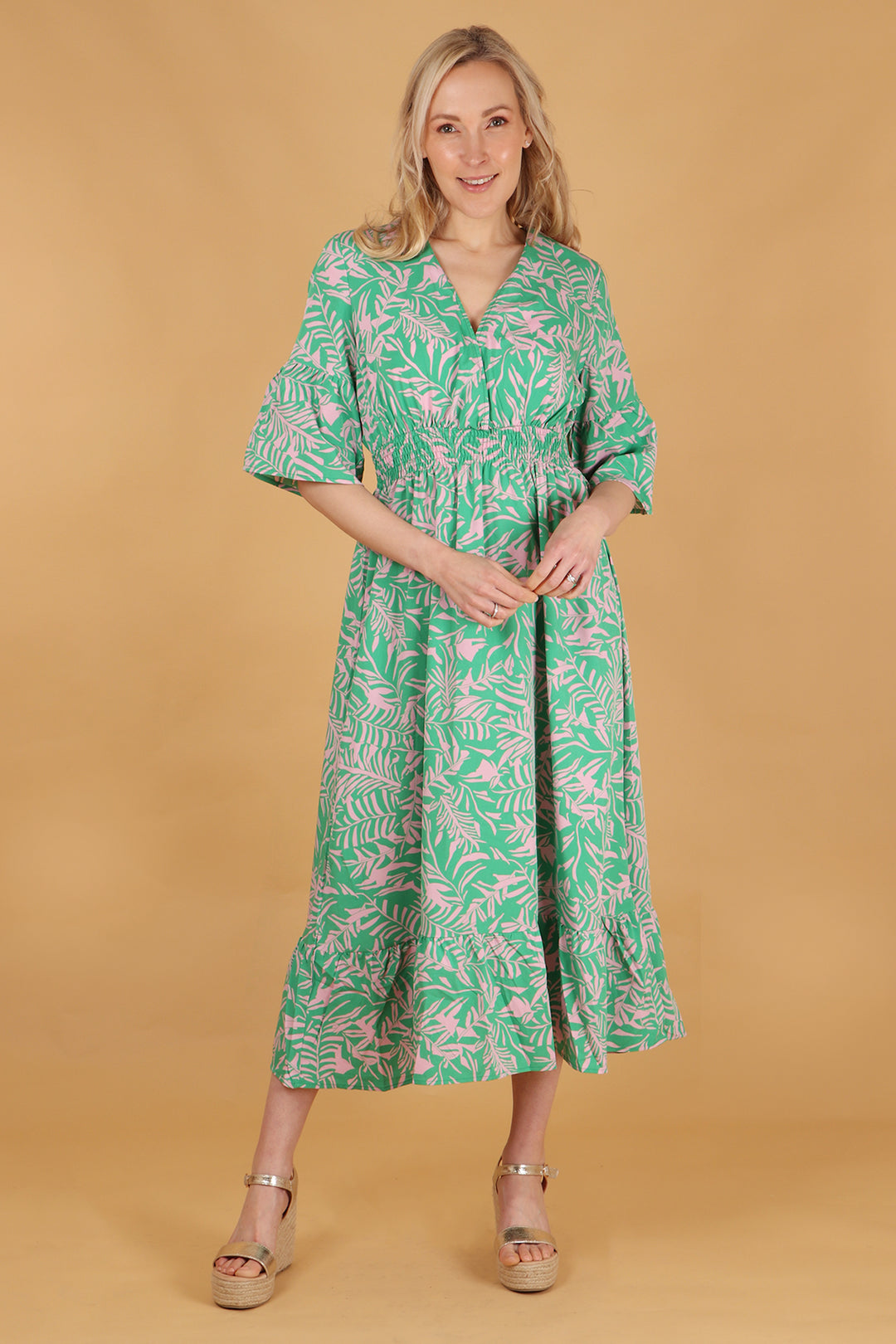 model wearing a maxi length tropical leaf print dress with 3/4 sleeves and a deep v neck 