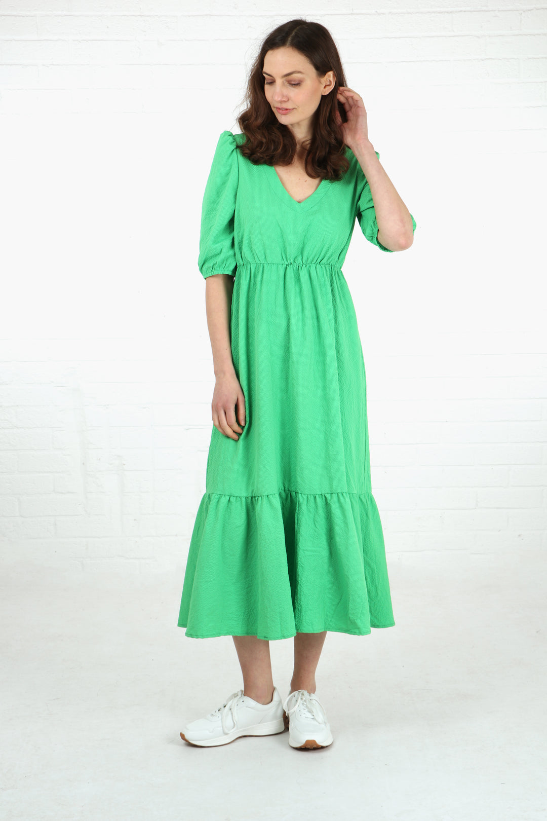 model wearing a textured green midi dress with elbow length puff sleeves and a tiered hem