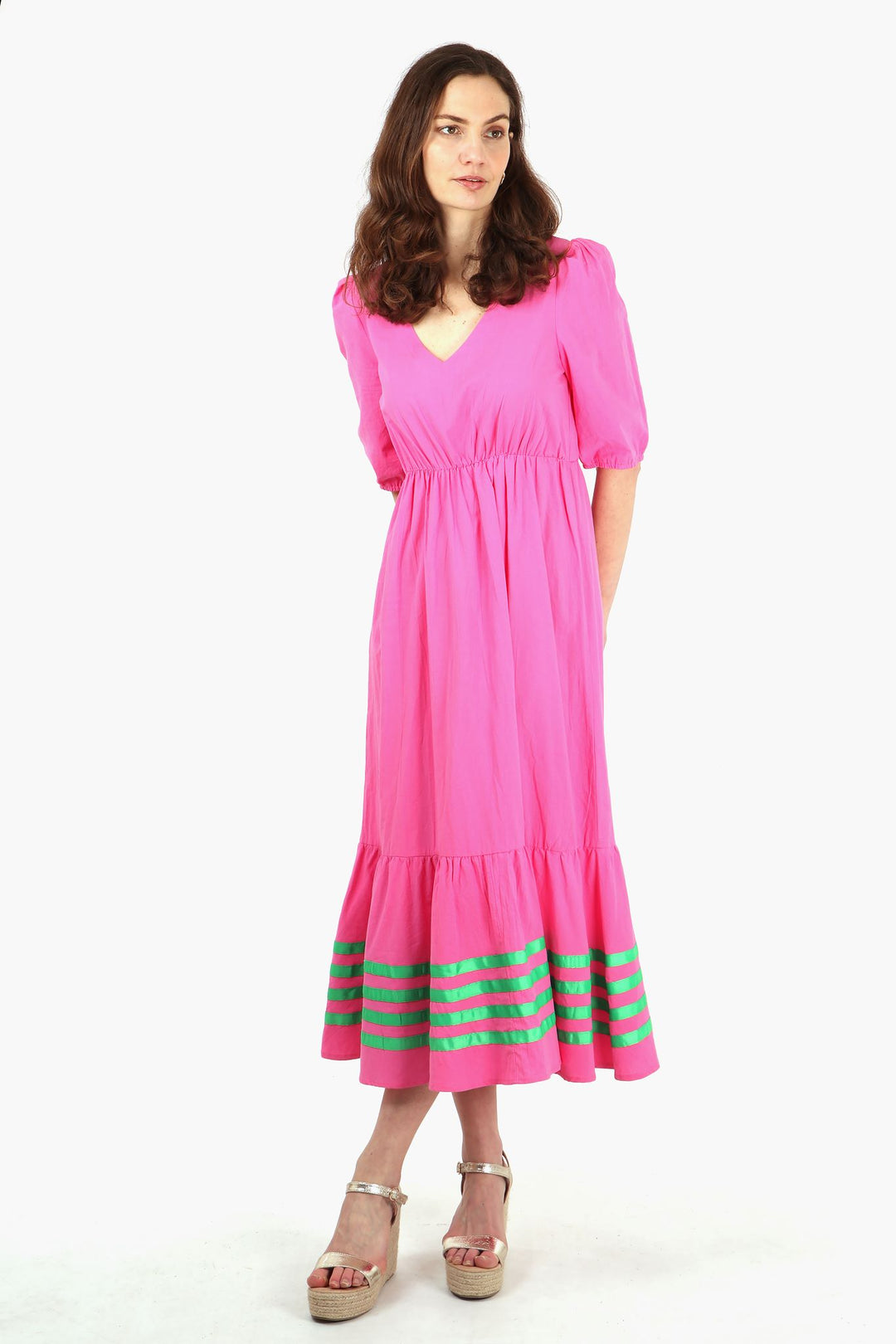 model wearing a pink midaxi length dress with four horizontal green ribbon stripes on the bottom tier of the dress, dress has a v neck and elbow length short sleeves