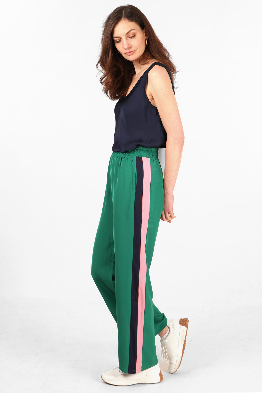 model wearing long green trousers with navy blue and pink stripe running the length of the leg at the side of the trousers
