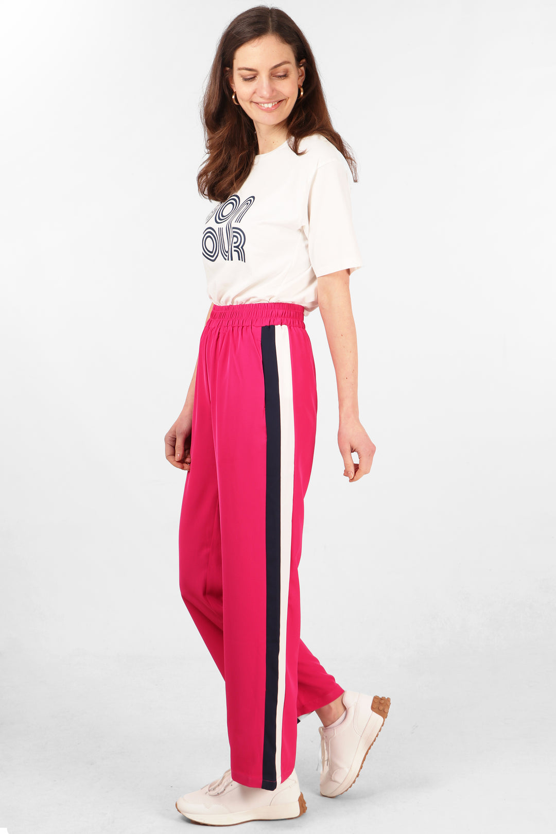 model wearing long pink trousers with navy blue and white stripe running the length of the leg at the side of the trousers