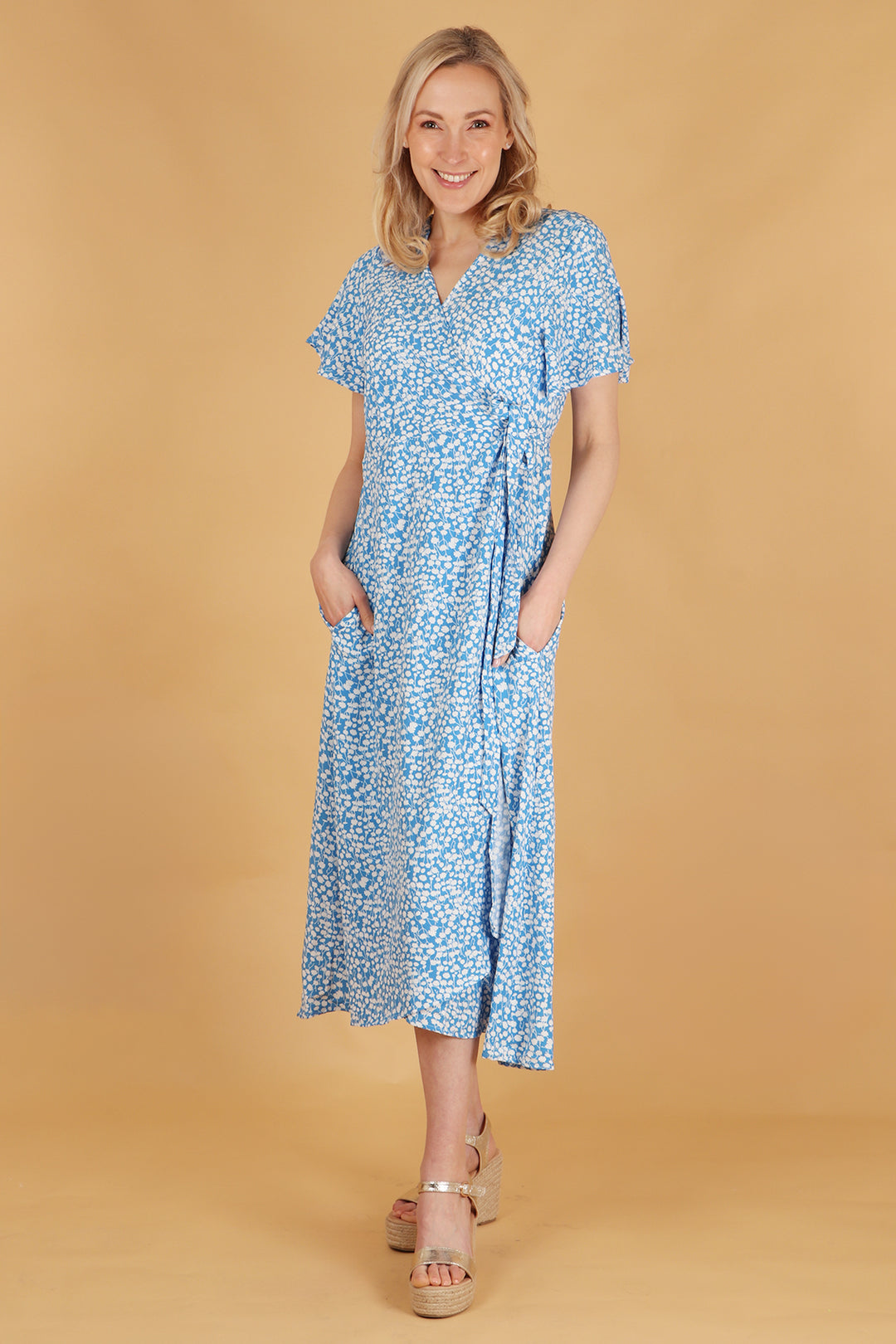 model wearing a blue and white ditsy floral pattern midi length wrap dress with a v neck and short sleeves