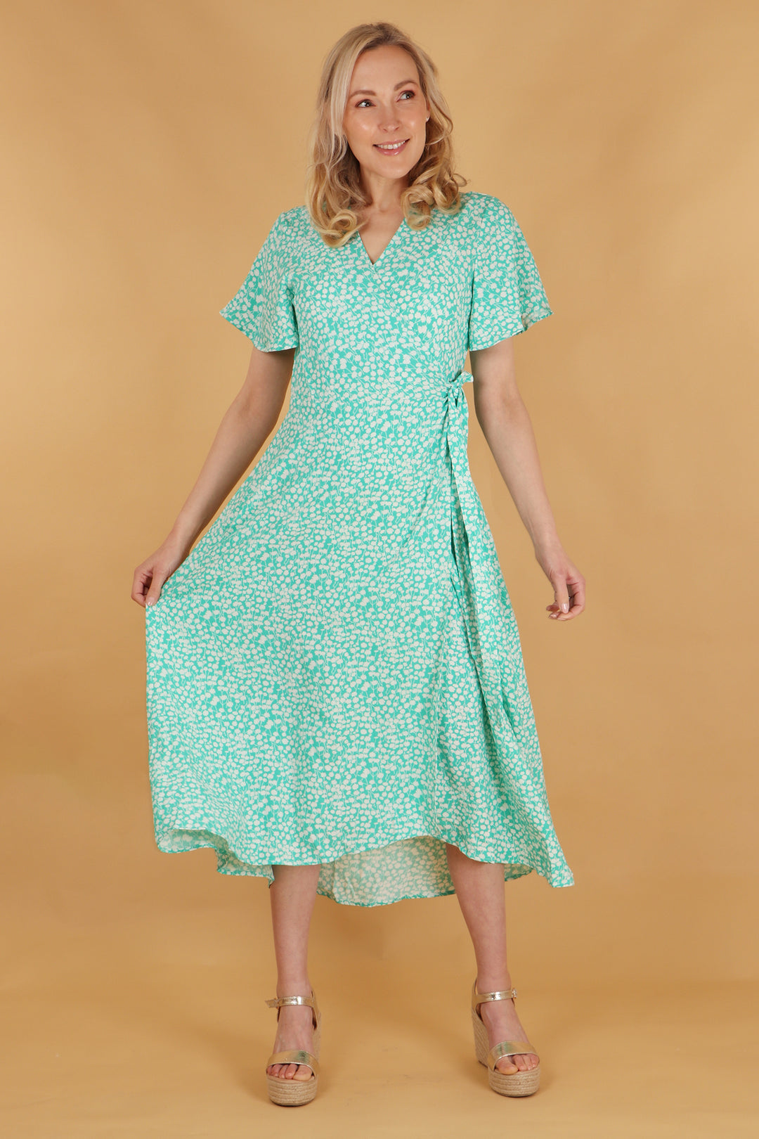 model wearing a green and white ditsy floral pattern midi length wrap dress with a v neck and short sleeves