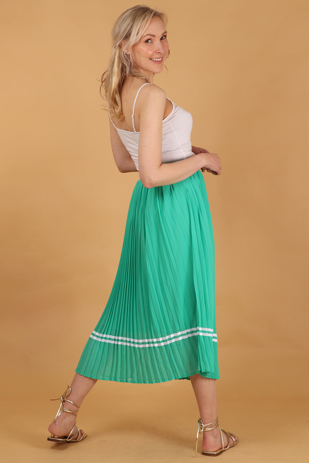 model showing the back of the green pleated skirt, showing the ribbon trim stripe is all around the skirt