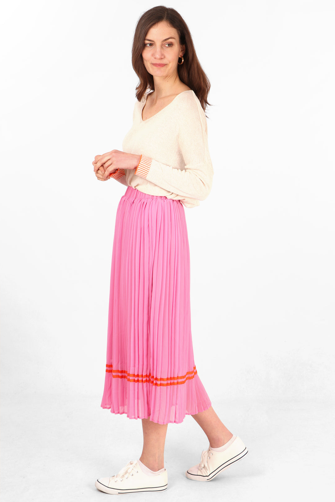 model wearing a pink pleated midi skirt with an orange ribbon stripe trim above the hem