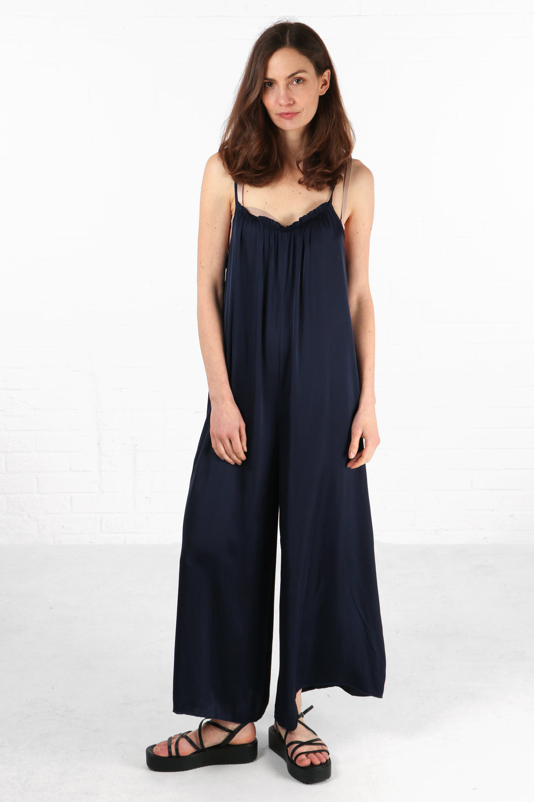 model wearing a navy blue faux silk wideleg jumpsuit with thin spaghetti straps and a v neck