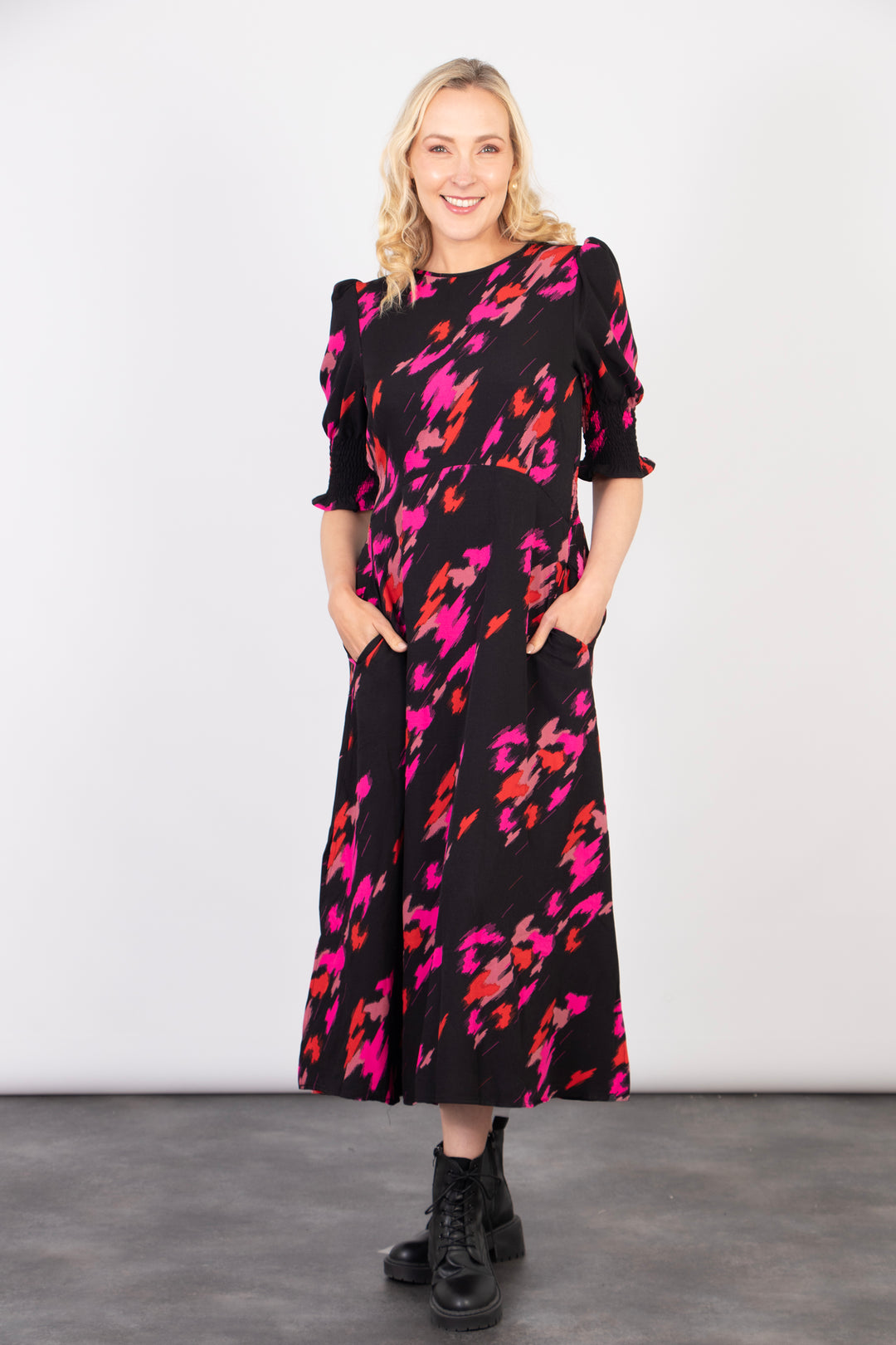 model showing that the black and fuchsia animal print tea dress has pockets on the front of the design