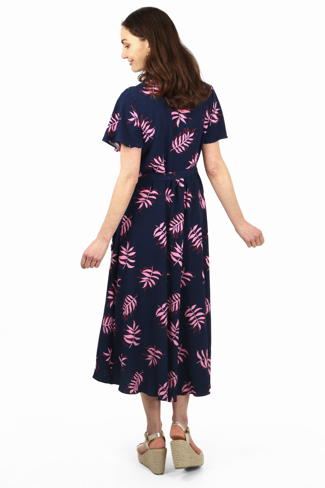 model showing the back of the wrap dress showing an all over navuy blue dress with a pattern of pink palm leaves