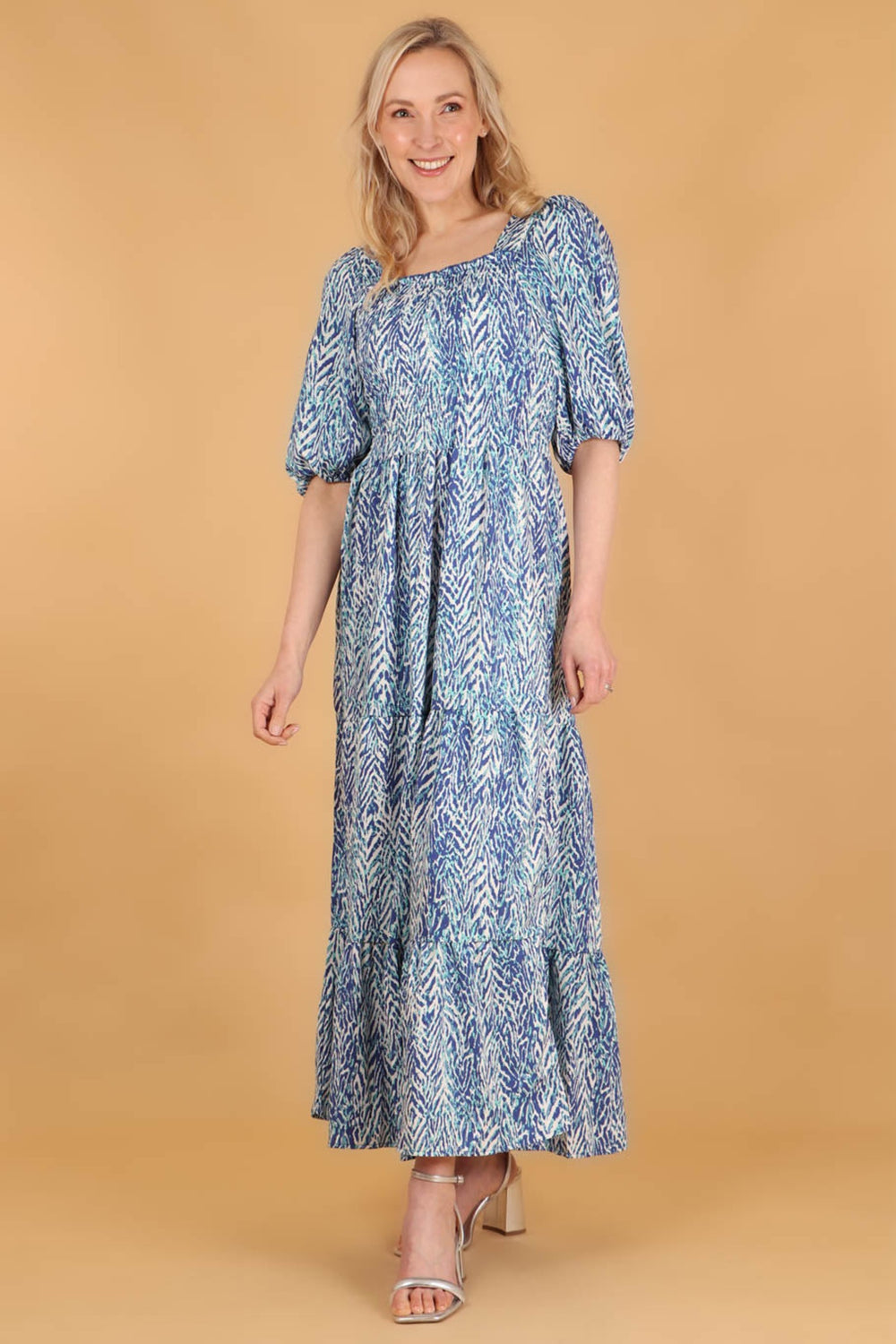 model wearing a blue chevron pattern maxi tiered milkmaid dress with a fully shirred bodice and 3/4 elbow length puff sleeves