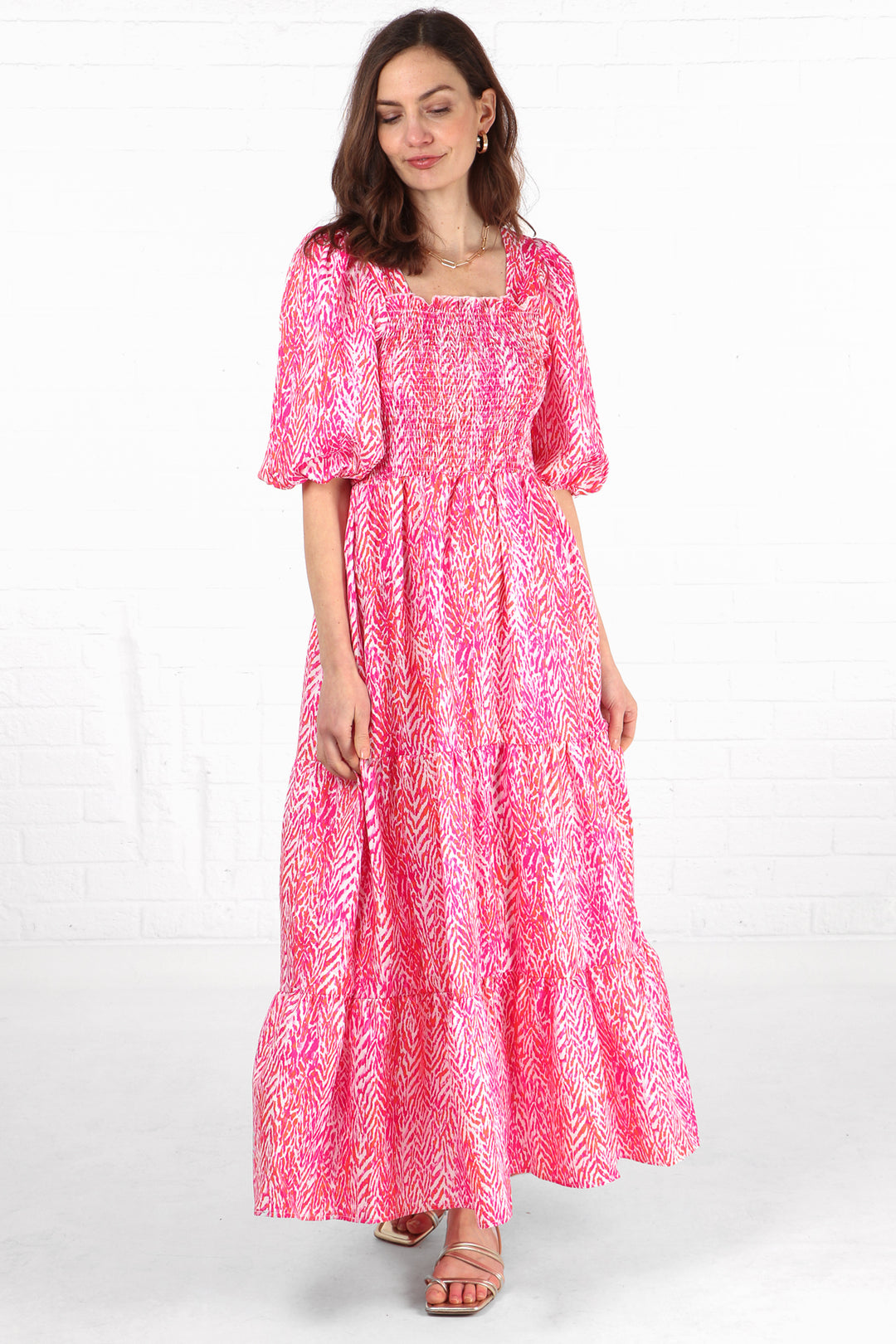 model wearing a pink chevron pattern tiered maxi dress with short puff sleeves and a shirred bodice