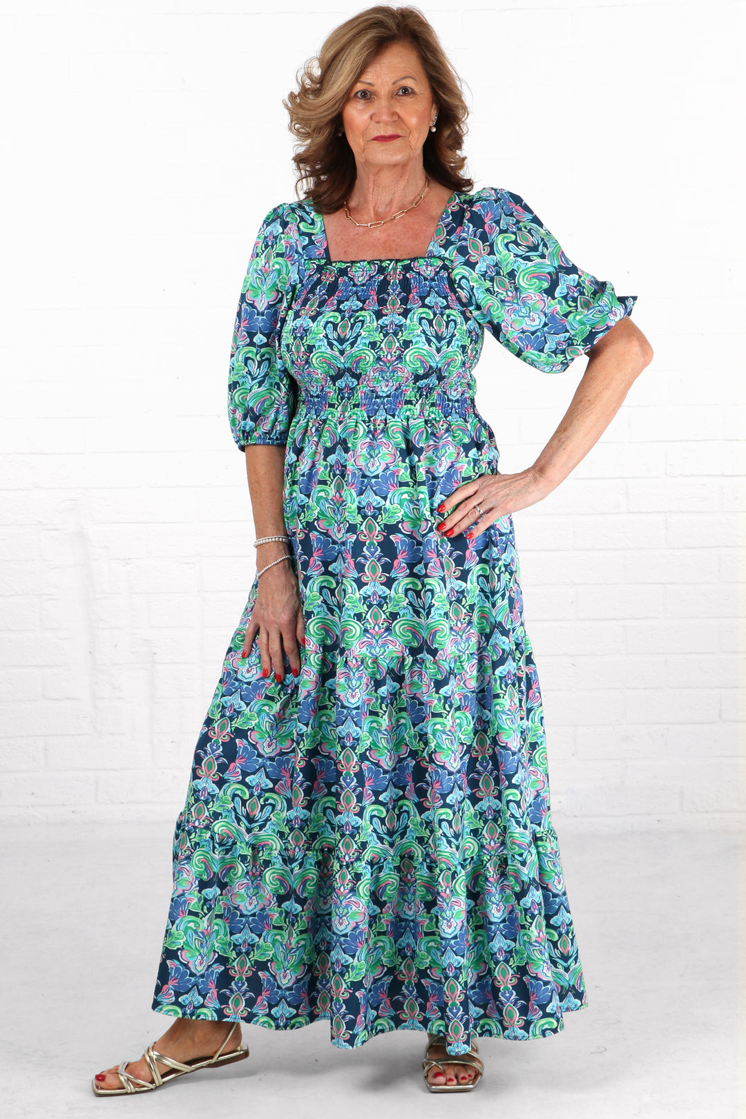 model wearing a blue tiered milkmaid maxi dress with short sleeves and an all over fleur de lis floral print