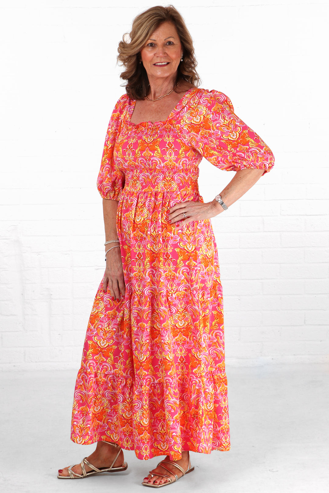 model wearing a pink and coral fleur di lis maxi milkmaid dress with 3/4 sleeves and a square neck line