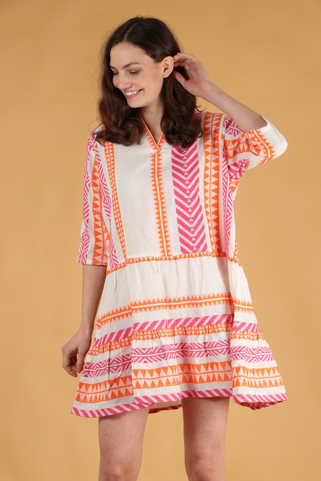 model wearing a cream, pink and orange midi dress with an aztec print pattern and 3/4 sleeves