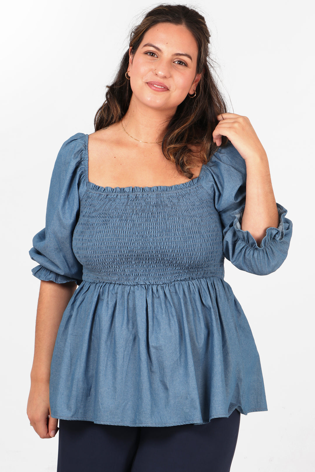model wearing a blue denim look peplum top with a square neckline and shirred bodice