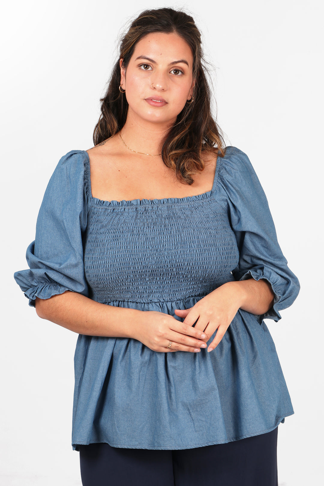 model wearing a denim blue peplum top with a shirred bodice, square neckline and 3/4 sleeves
