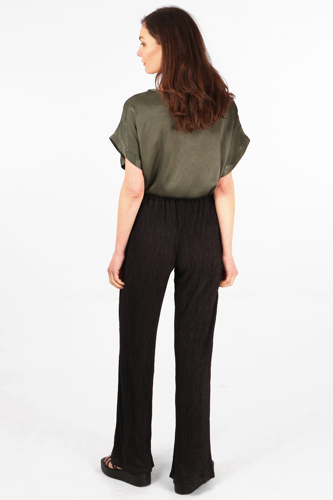 model showing the back of the black plisse trousers, showing an all over plisse fabric