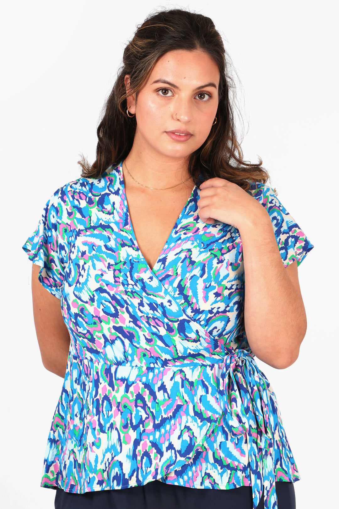 model wearing an abstract print short sleeved wrap top in blue with a waist tie and v neck