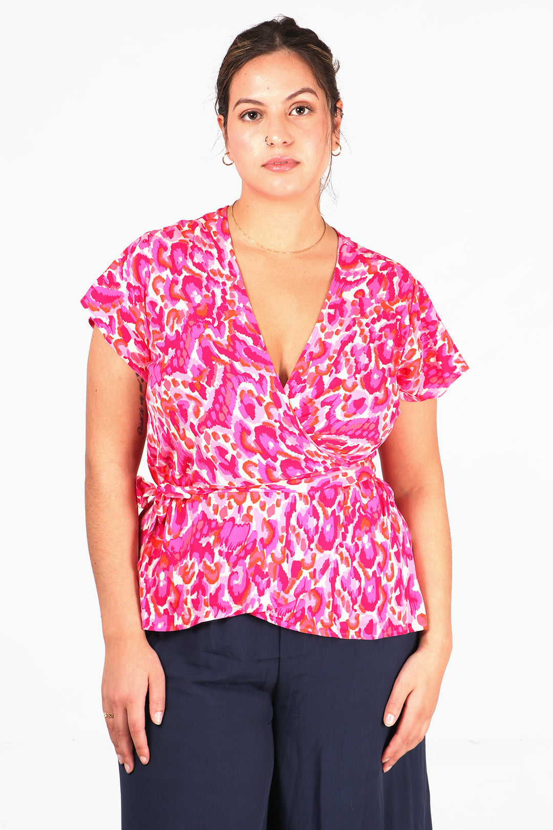 model wearing a pink abstract print wrap top with short angel sleeves and a v neck