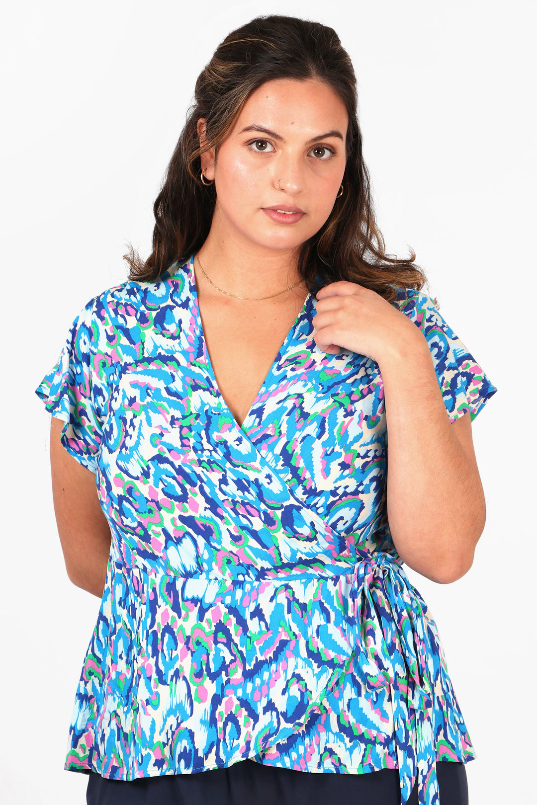 model wearing a blue abstract print v neck blouse with short sleeves and a waist tie