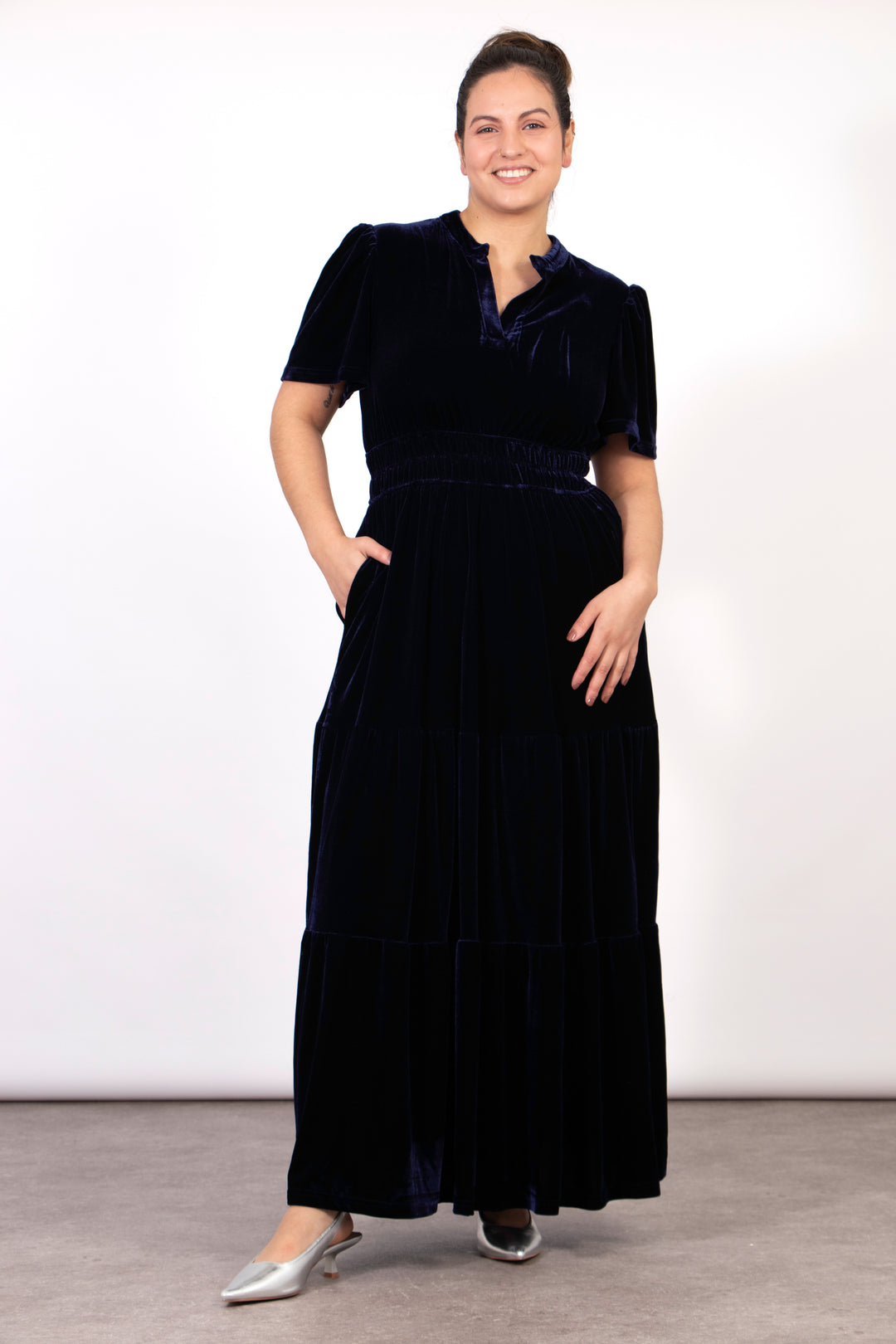 model wearing a short sleeve navy blue tiered velvet maxi dress . the dress has a cinched elasticated waist