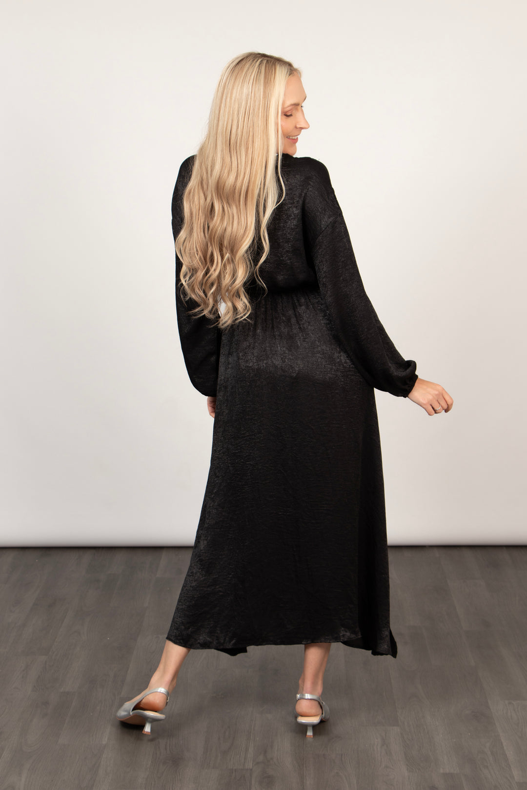 model showing the back of the long sleeve dress, highlighting the midi length and black metallic fabric