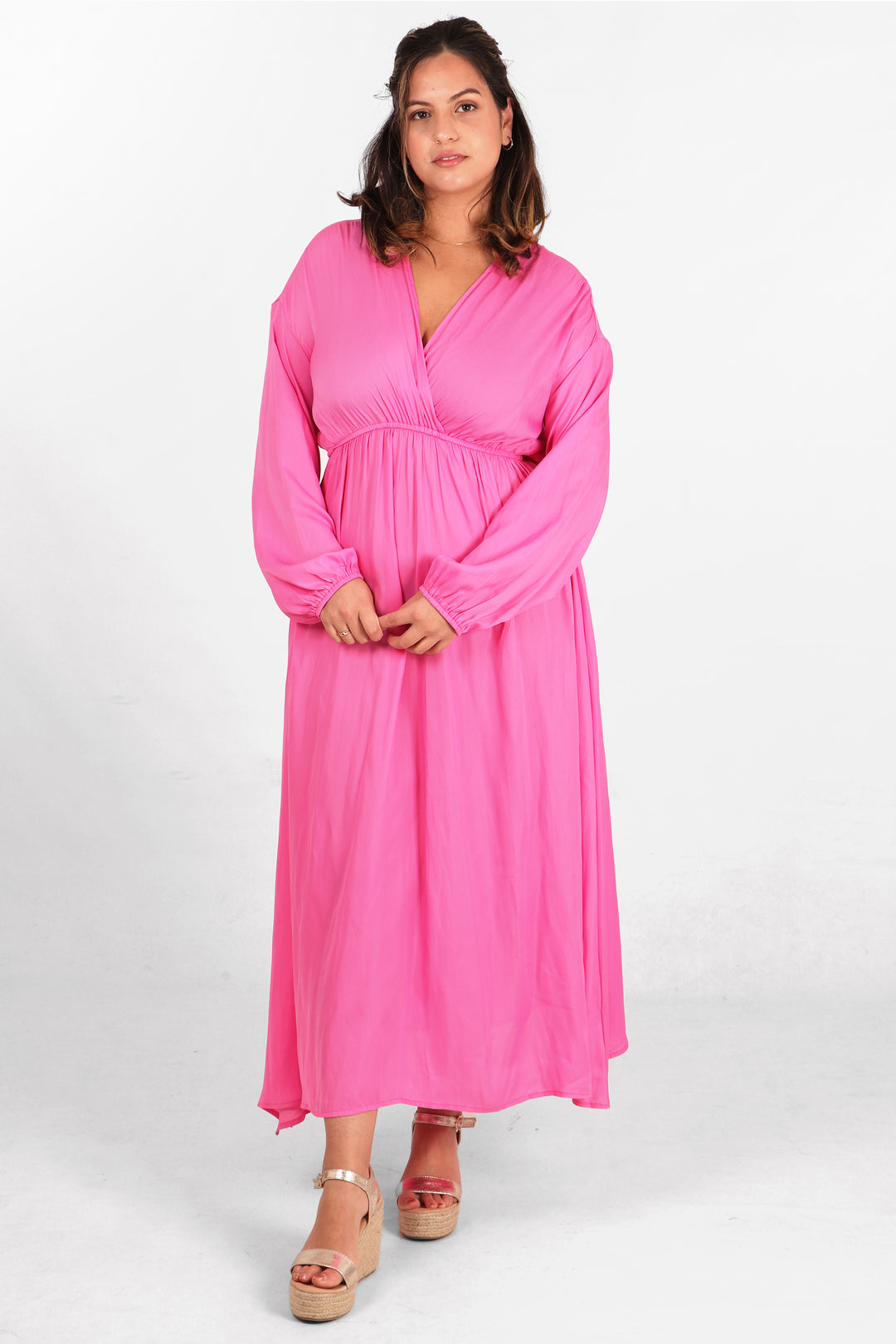 model wearing a plain pink long sleeved maxi dress with a faux wrap top and v neck