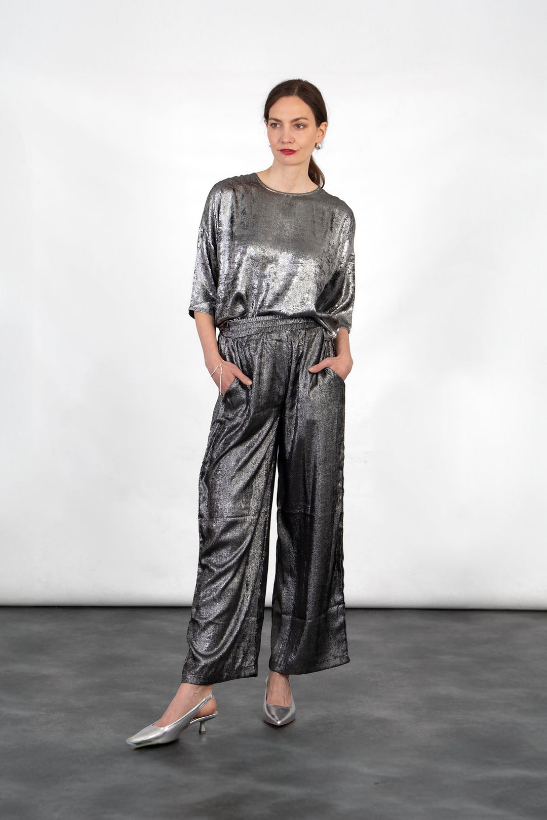 model wearing a pair of textured silver metallic trousers with an elasticated shirred waist and pockets