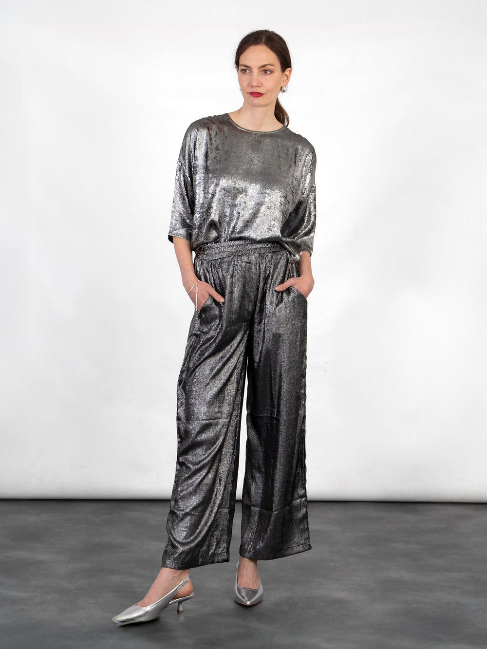 model wearing a pair of textured silver metallic trousers with an elasticated shirred waist and pockets