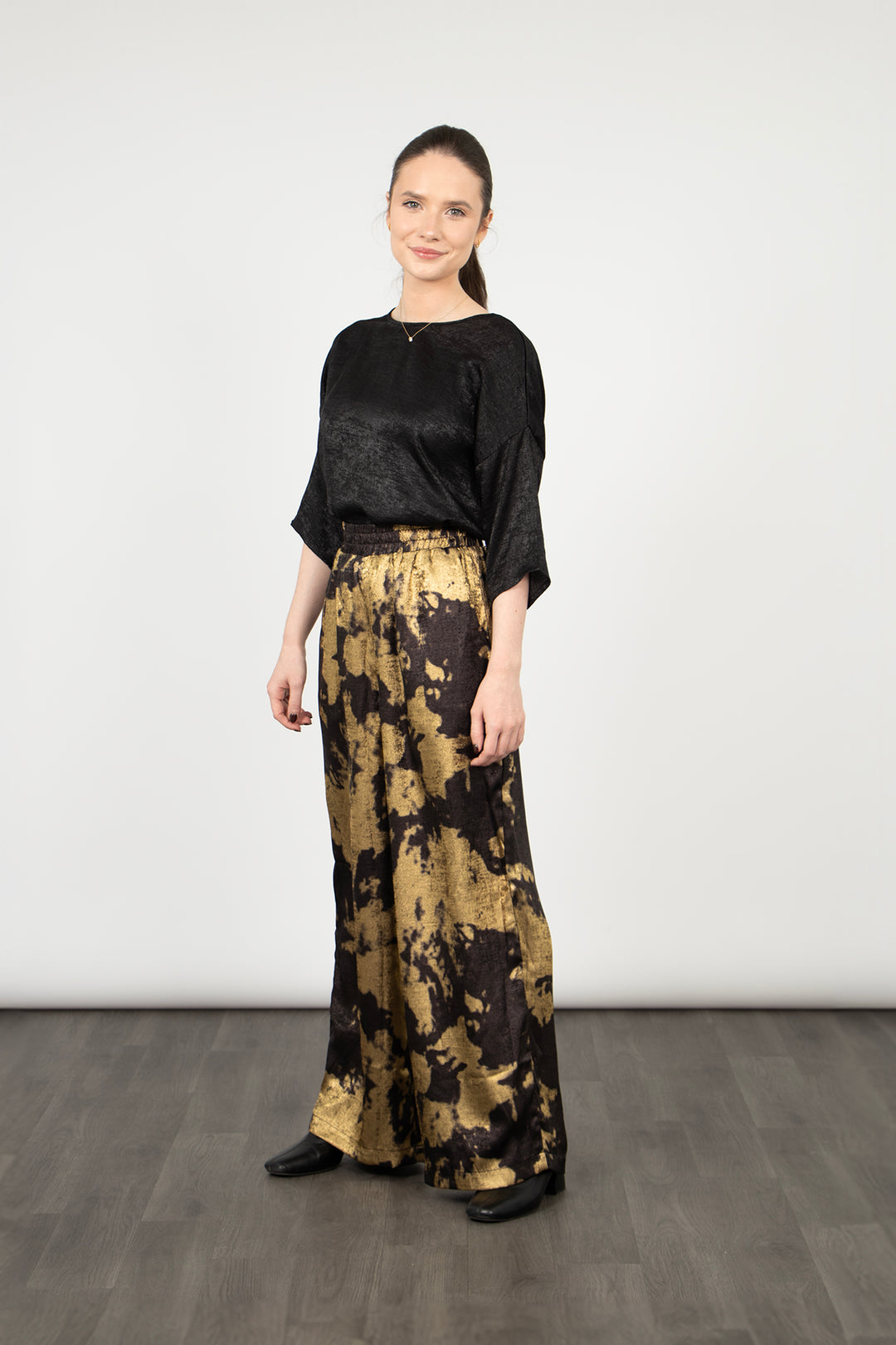 model wearing black and gold paint splash pattern wide leg trousers with a metallic sheen