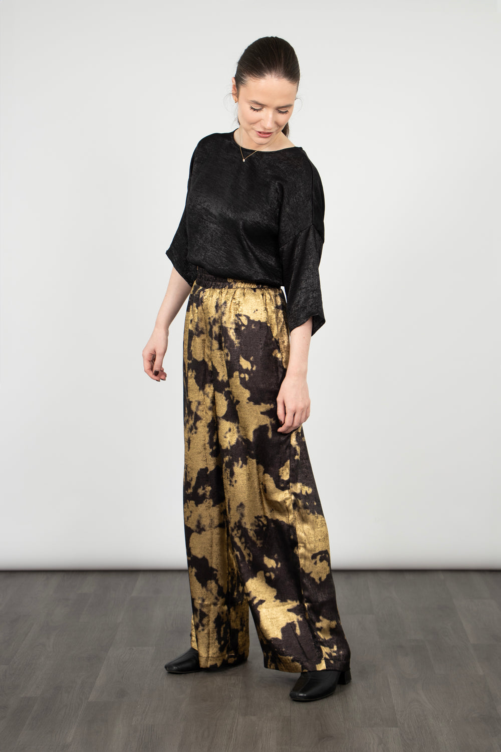 model wearing black and gold paint splash pattern wide leg trousers with a metallic sheen