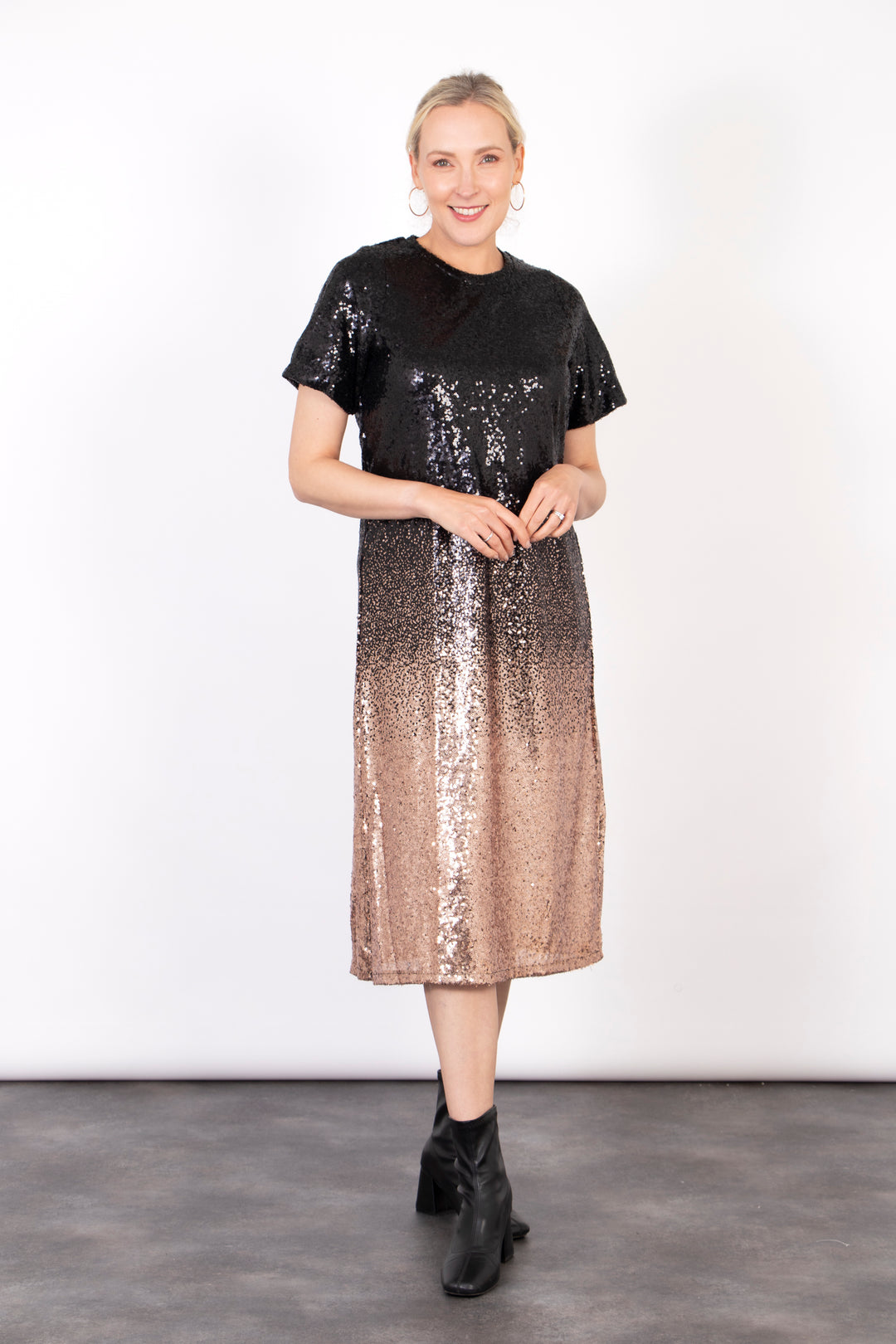 model wearing a black and bronze ombre sequin midi t-shirt dress. the dress falls just below the knee and has short sleeves and a round neck. there is an all over sequin shimmer