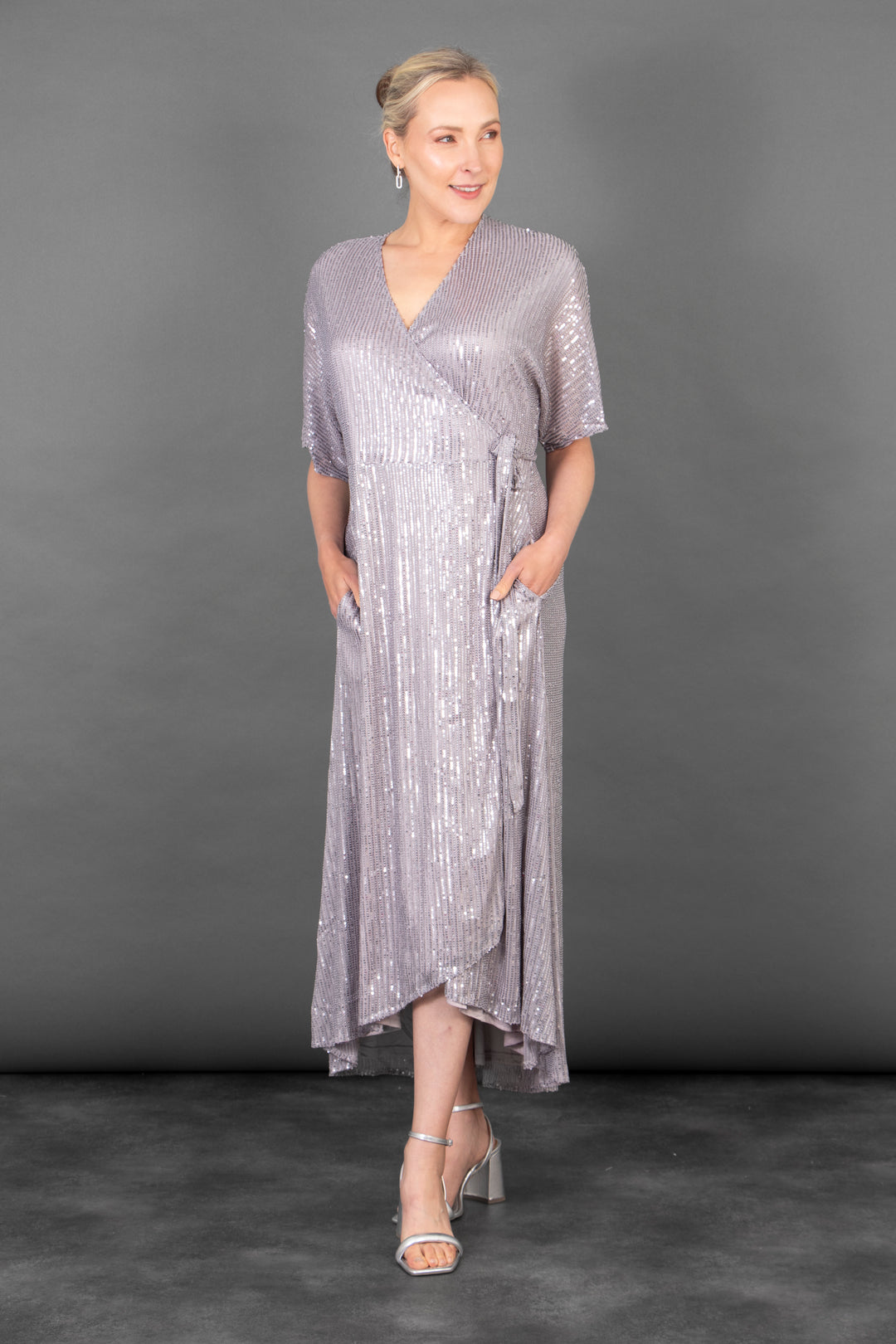 model wearing a silver sequin short sleeve wrap dress, the dress has a v-neck and pockets