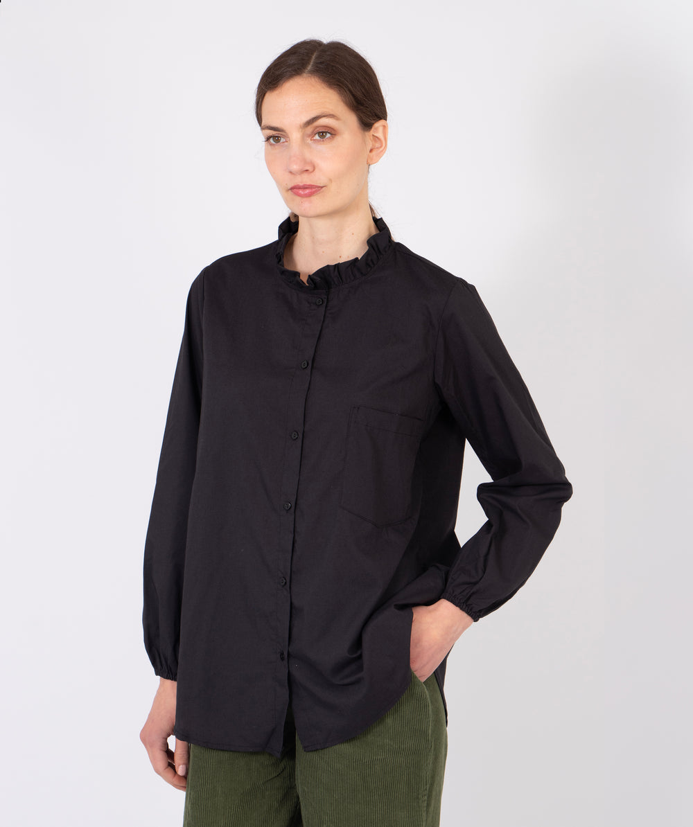 model wearing a plain black relaxed fitting cotton shirt with a frilled collar and long sleeves.