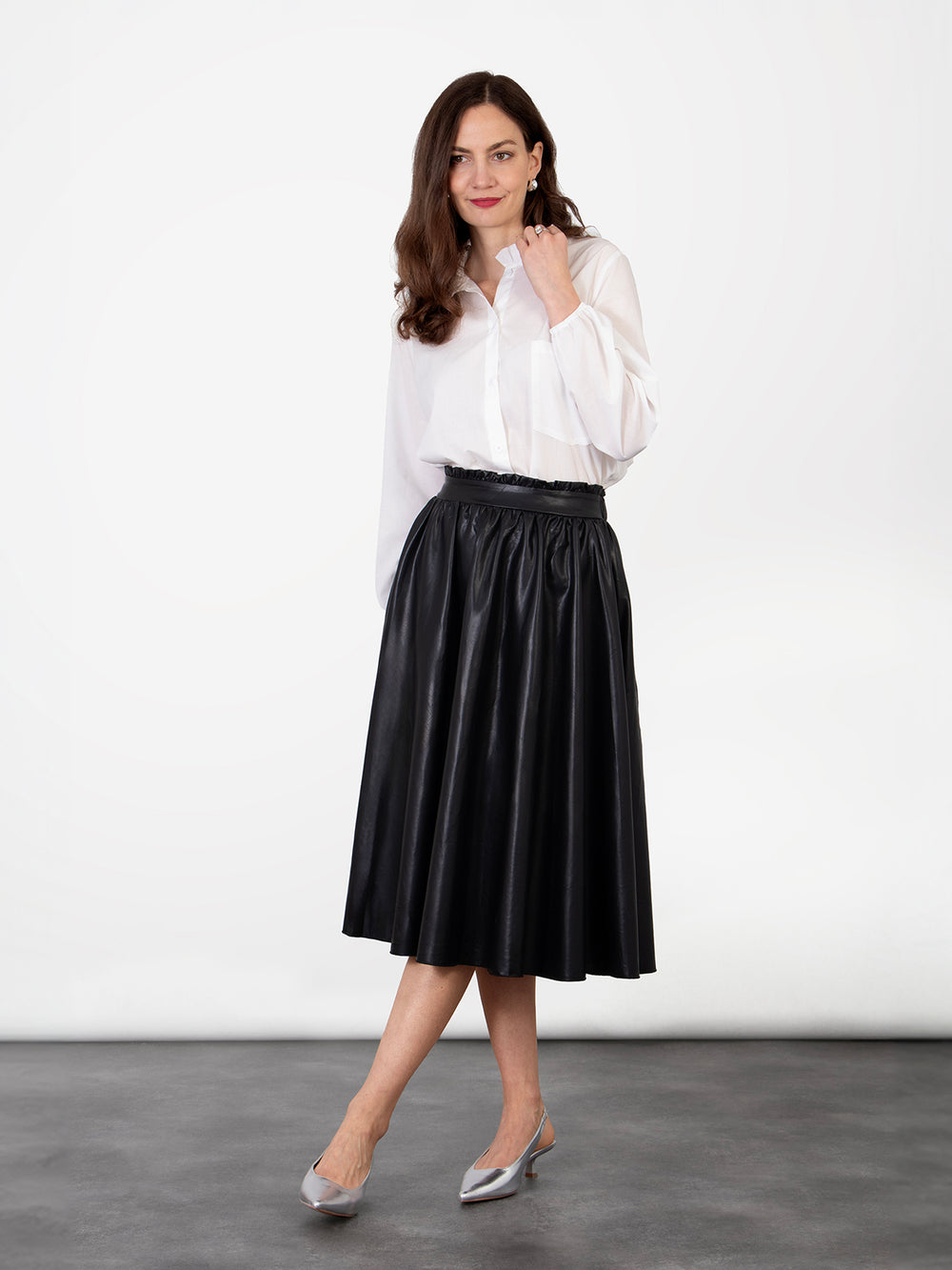 model wearing a plain black faux leather ruffled midi skirt, the skirt is a-line in shape