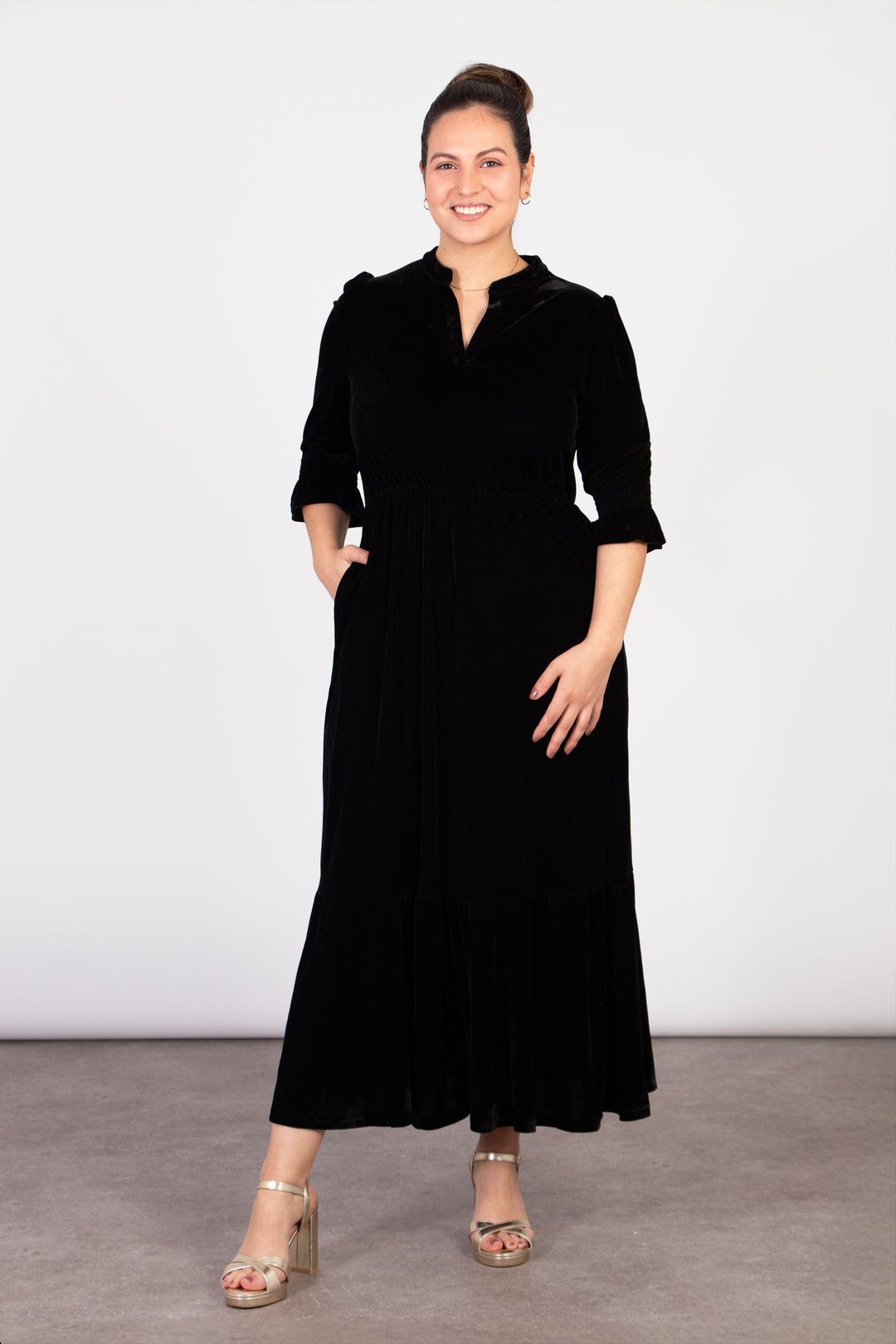 model wearing a midi length black velvet dress. the dress has pockets on the side of the design
