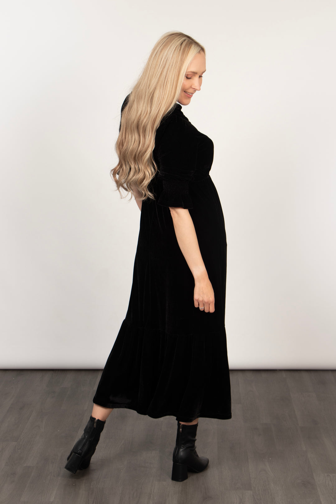 model showing the back of the black velvet tiered dress, showing the elbow length sleeves and the midi length hem
