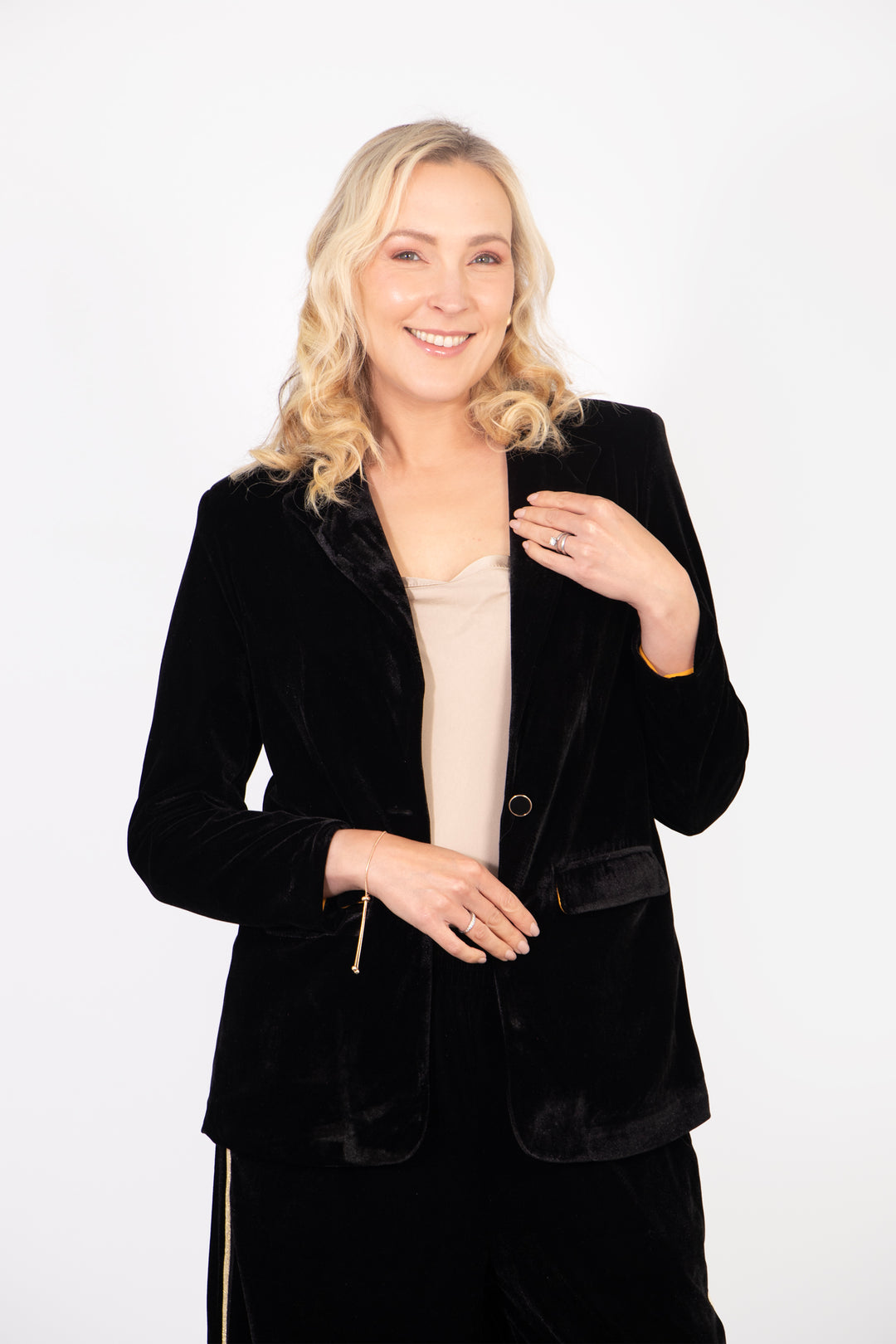 model wearing a plain black velvet blazer, accessorised with a gold vest top and black velvet trousers. the jacket has long sleeves and a button fastening at the front