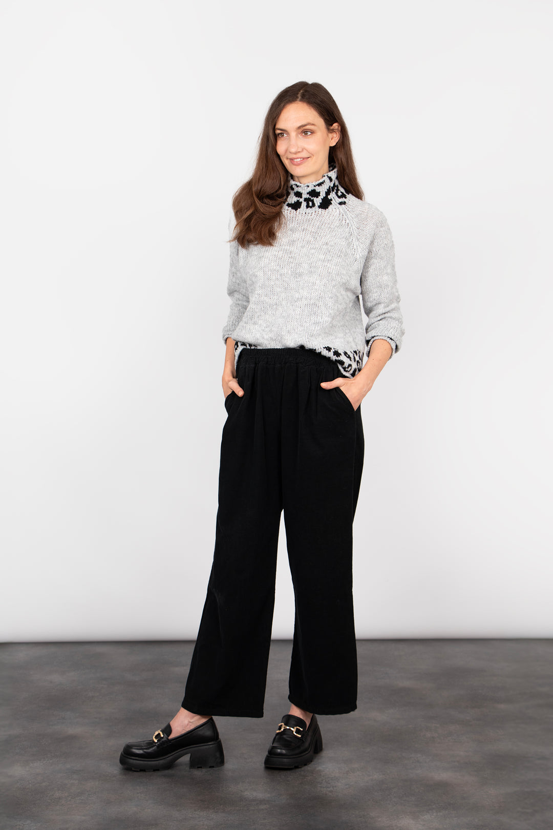 model wearing black baby cord trousers accessorised with black shoes and a grey leopard print jumper