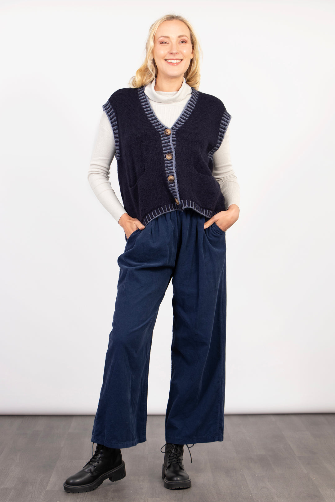 model wearing blue cord trousers accessorised with a blue knitted vest top. the trousers have pockets on the front and a wide leg design