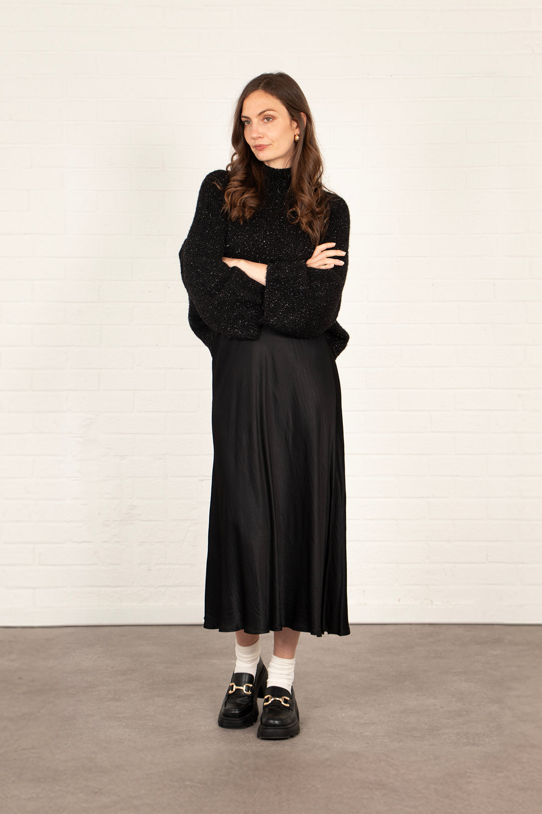 model wearing a plain black silky midi slip skirt, accessorised with a winter jumper and black shoes.