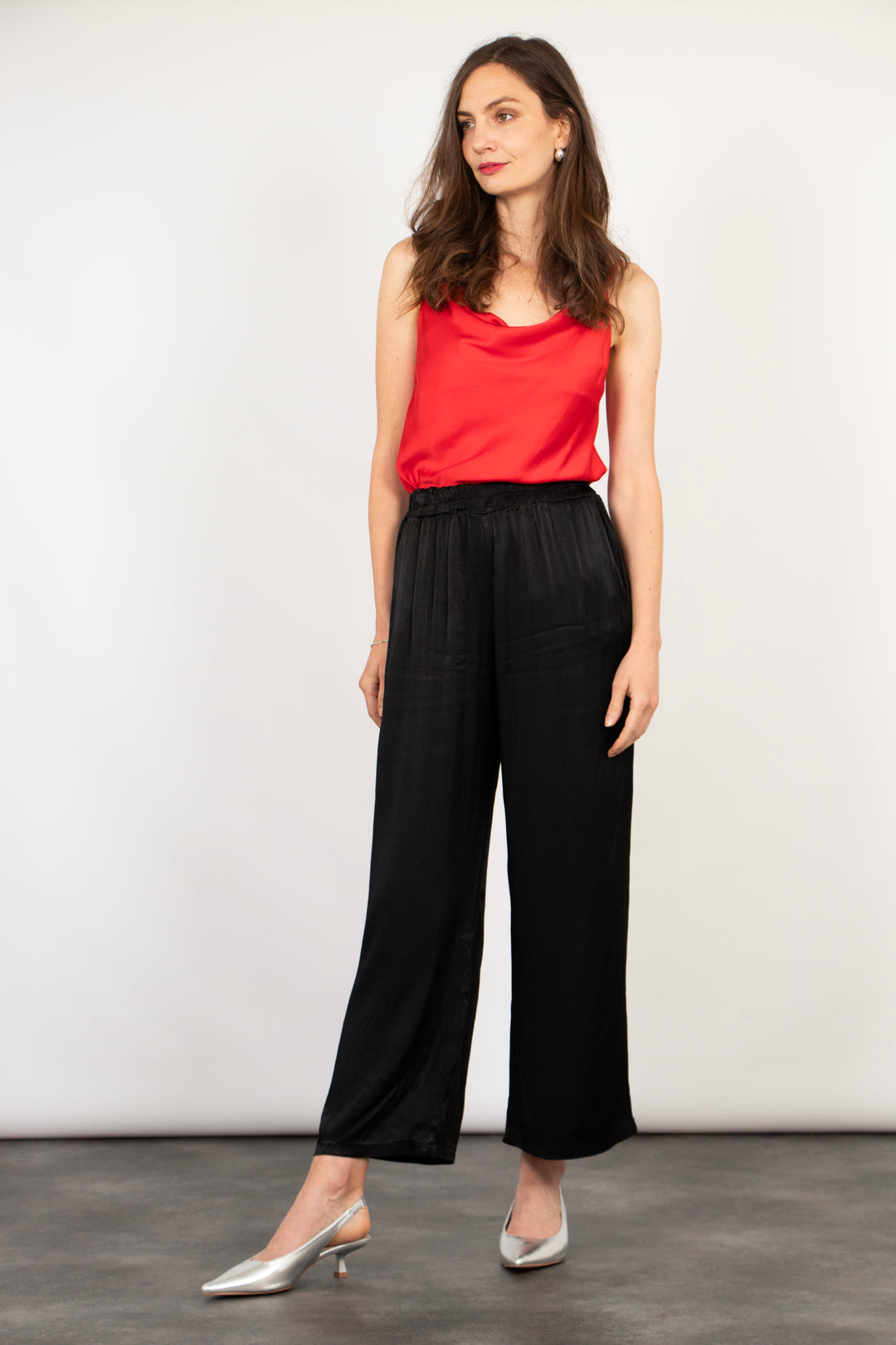 model wearing black wide leg trousers accessorised with silver kitten heels and a red vest top, the trousers are relaxed fitting and have an elasticated waist