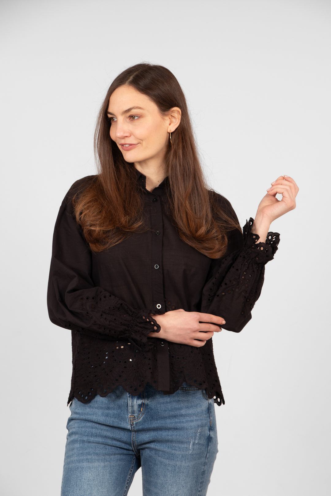 model wearing a lightweight black cotton shirt with a detailed broderie anglaise design on the cuffs and lower quarter of the bodice.