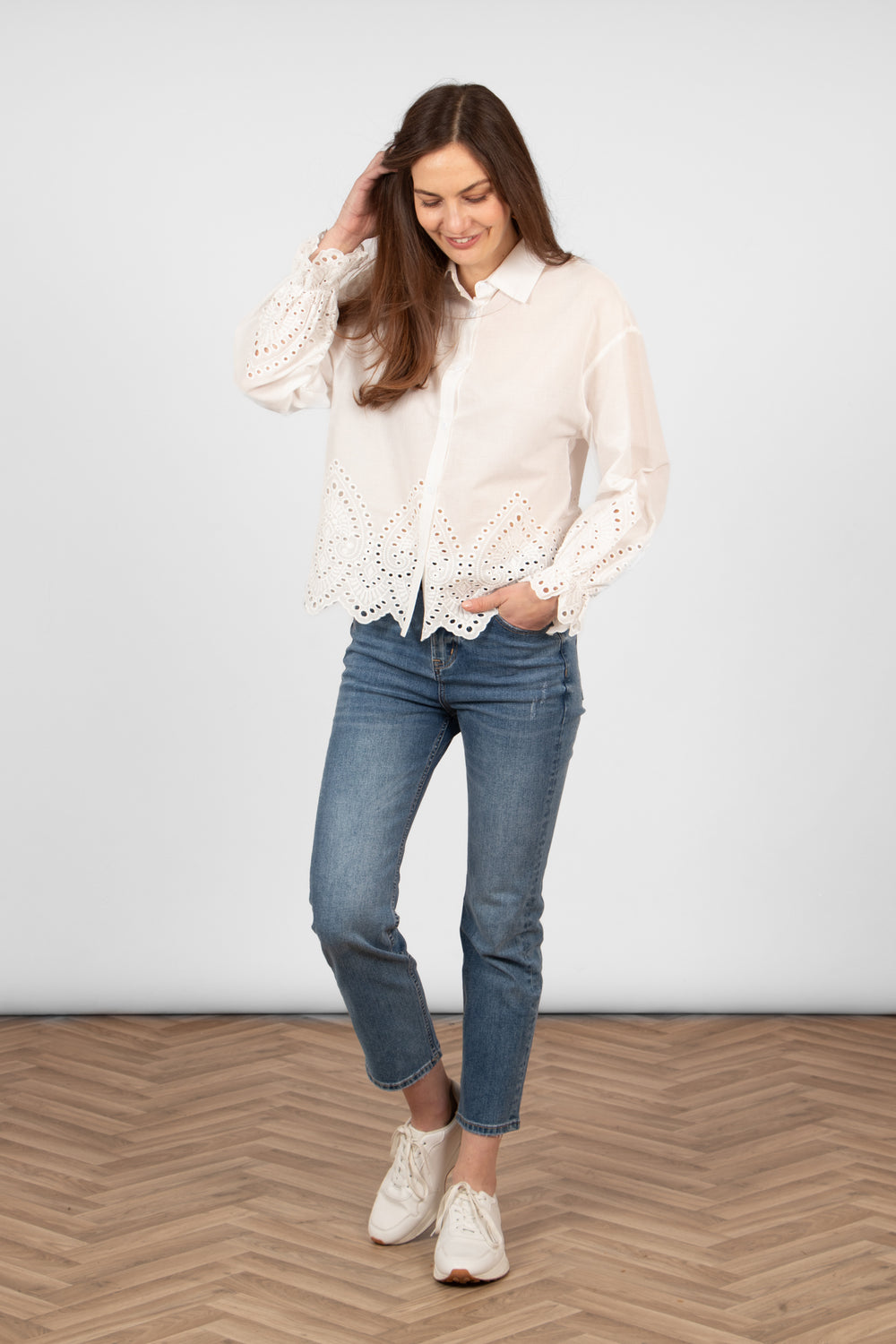 model wearing a white cotton broderie anglaise shirt styled with casual blue jeans and white trainers