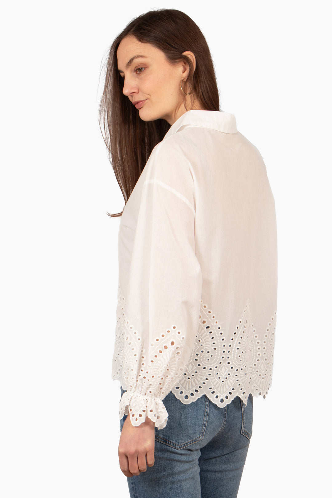 model showing the back of the blouse, the broderie design goes all the way around the piece. the hemline is scalloped and the sleeve cuffs are frilly with the broderie pattern.