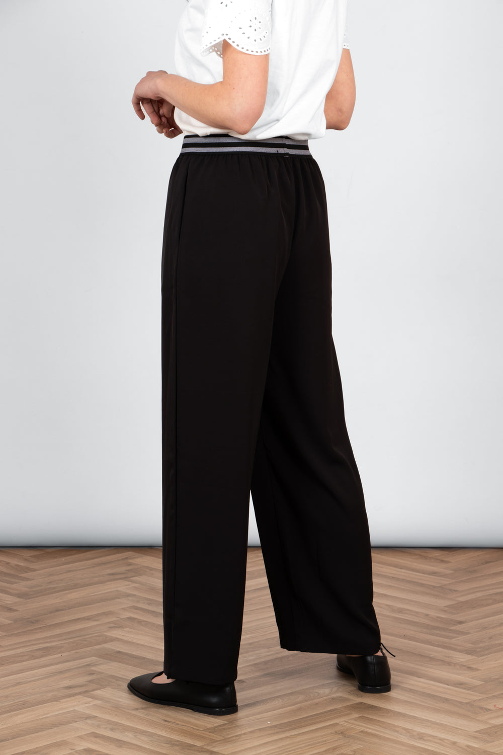 model wearing a pair of full length black wide leg trousers with a striped elasticated waistband. the waistband features two horizontal grey stripes.