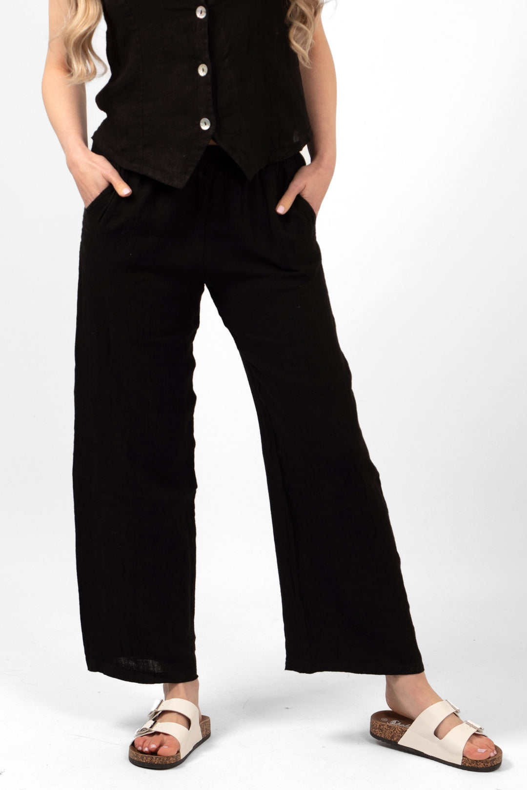 model wearing a pair of plain black wide leg linen trousers. the trousers have pockets and an elasticated waist.