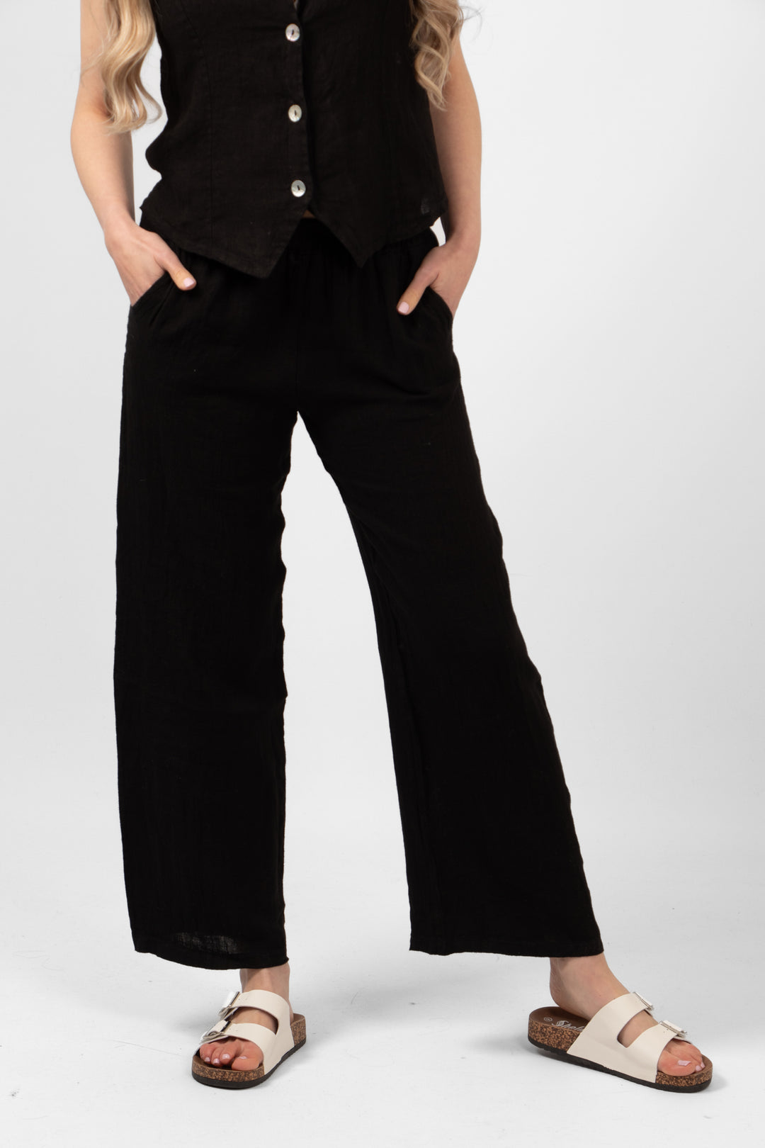 model wearing a pair of plain black wide leg linen trousers. the trousers have pockets and an elasticated waist.