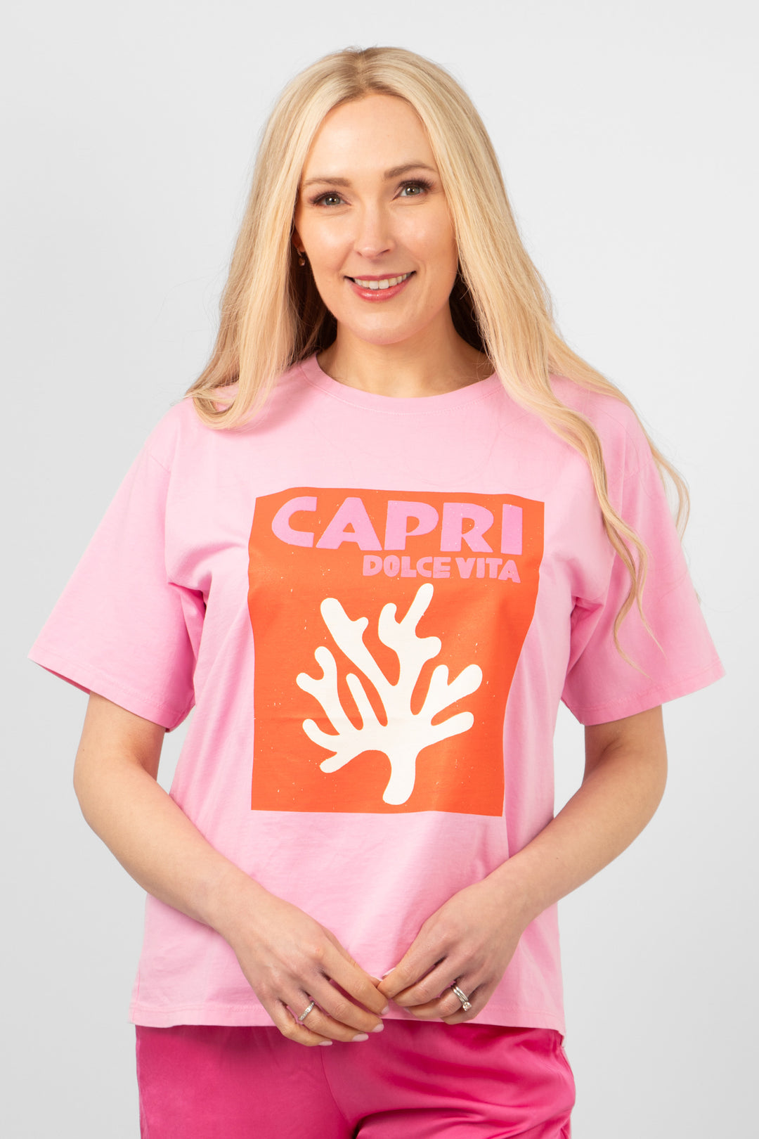 model wearing a hot pink tshirt with a coral graphic motif on the front which says capri dolce vita. the tshirt has a round neck and loose fitting short sleeves