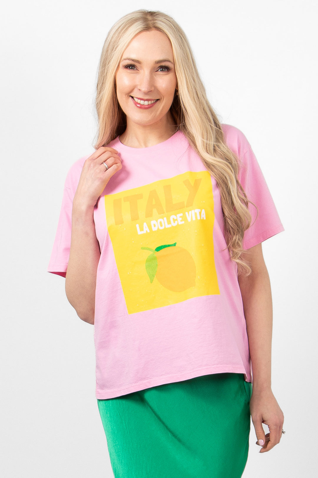 model wearing a light pink tshirt with a yellow graphic motif on the front which says Italy la dolce vita. the tshirt has a round neck and loose fitting short sleeves