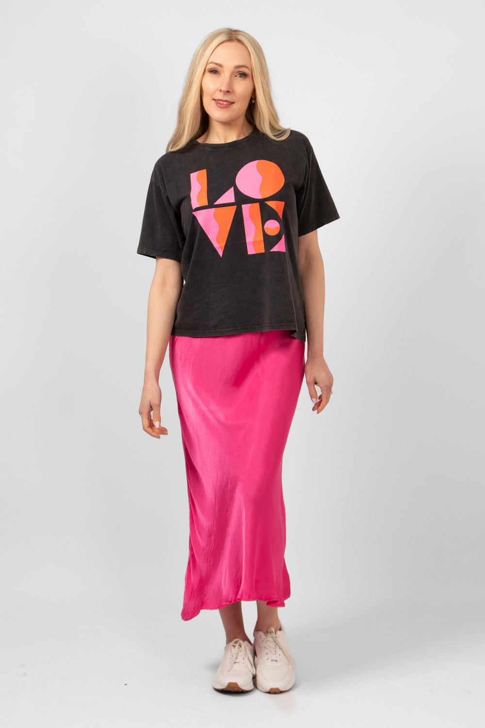 model wearing the black t-shirt with the love graphic design styled with a pink midi slip skirt and white trainers.